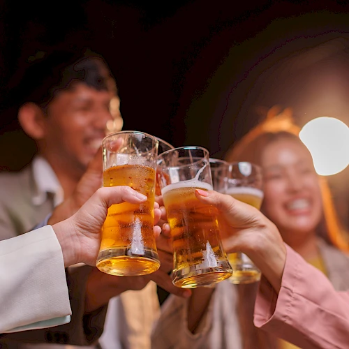 A group of people cheers with beer cups in a festive party, drinks clinking in a celebratory toast at night.