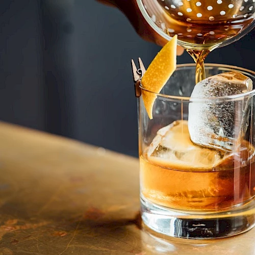 A whiskey on the rocks with a lemon twist, as a drink being poured into a glass.