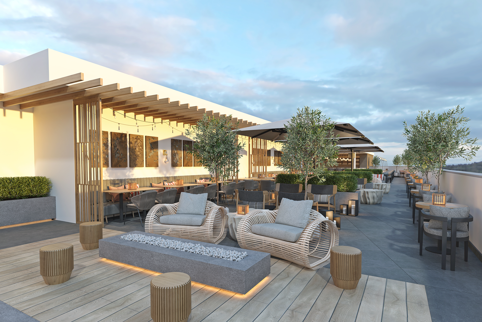 A rooftop terrace with modern seating, tables, plants, and ambient lighting under a partly cloudy sky.