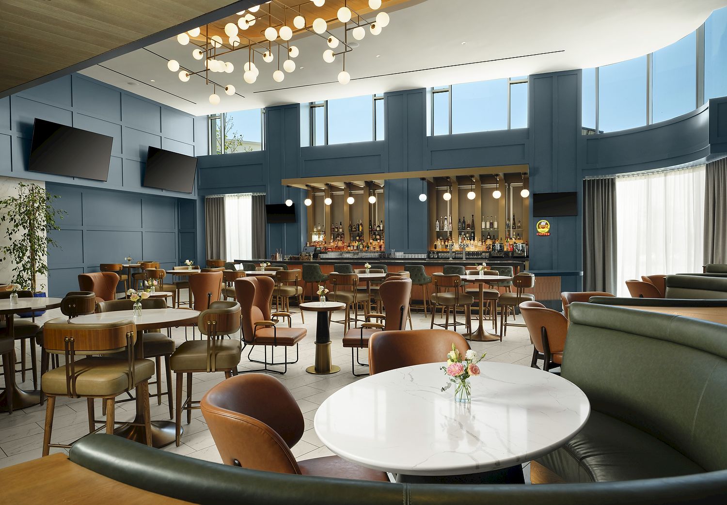Modern lounge/bar with teal walls, pendant globe lights, stools, and a back bar lined with bottles and coffee signage.