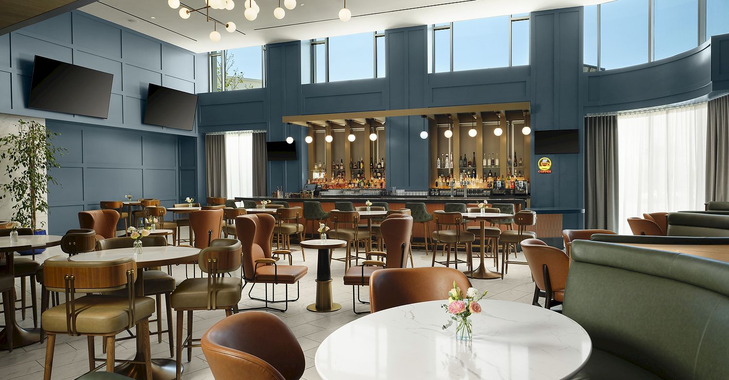 Modern lounge/bar with teal walls, pendant globe lights, stools, and a back bar lined with bottles and coffee signage.