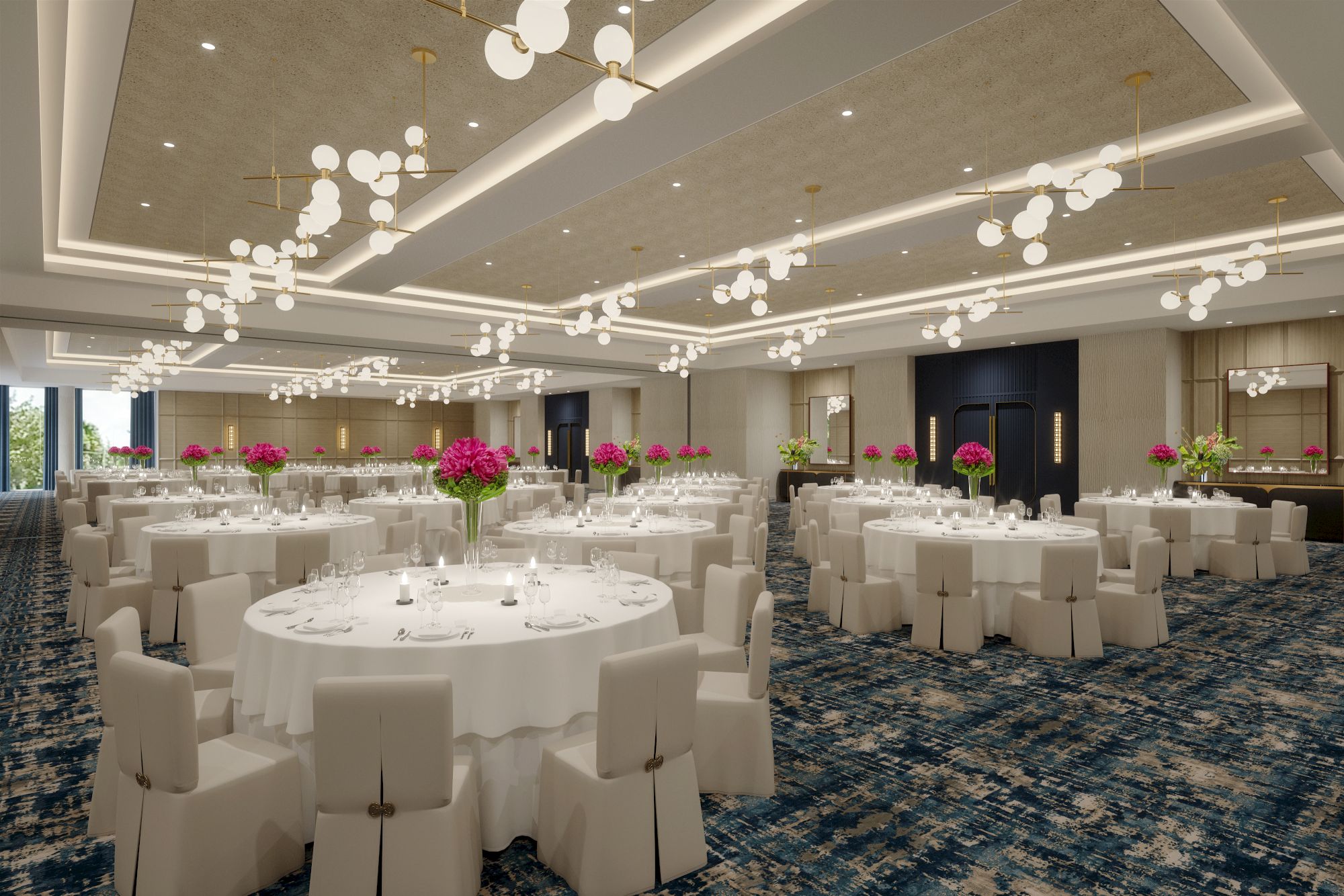 The image shows a spacious banquet hall with round tables, white tablecloths, chairs, elegant chandeliers, and floral centerpieces on tables.