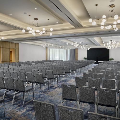 An empty conference hall with rows of gray chairs and hanging globe chandeliers.