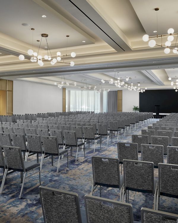 An empty conference hall with rows of gray chairs and hanging globe chandeliers.