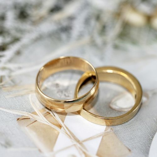 Two gold wedding rings are placed on a decorative surface with a soft, neutral background.