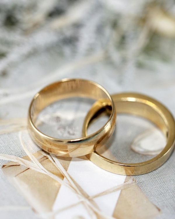 Two gold wedding rings are placed on a decorative surface with a soft, neutral background.