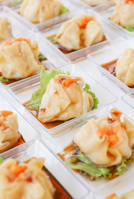The image shows rows of dumplings, each in a small container on a bed of lettuce and topped with a garnish.