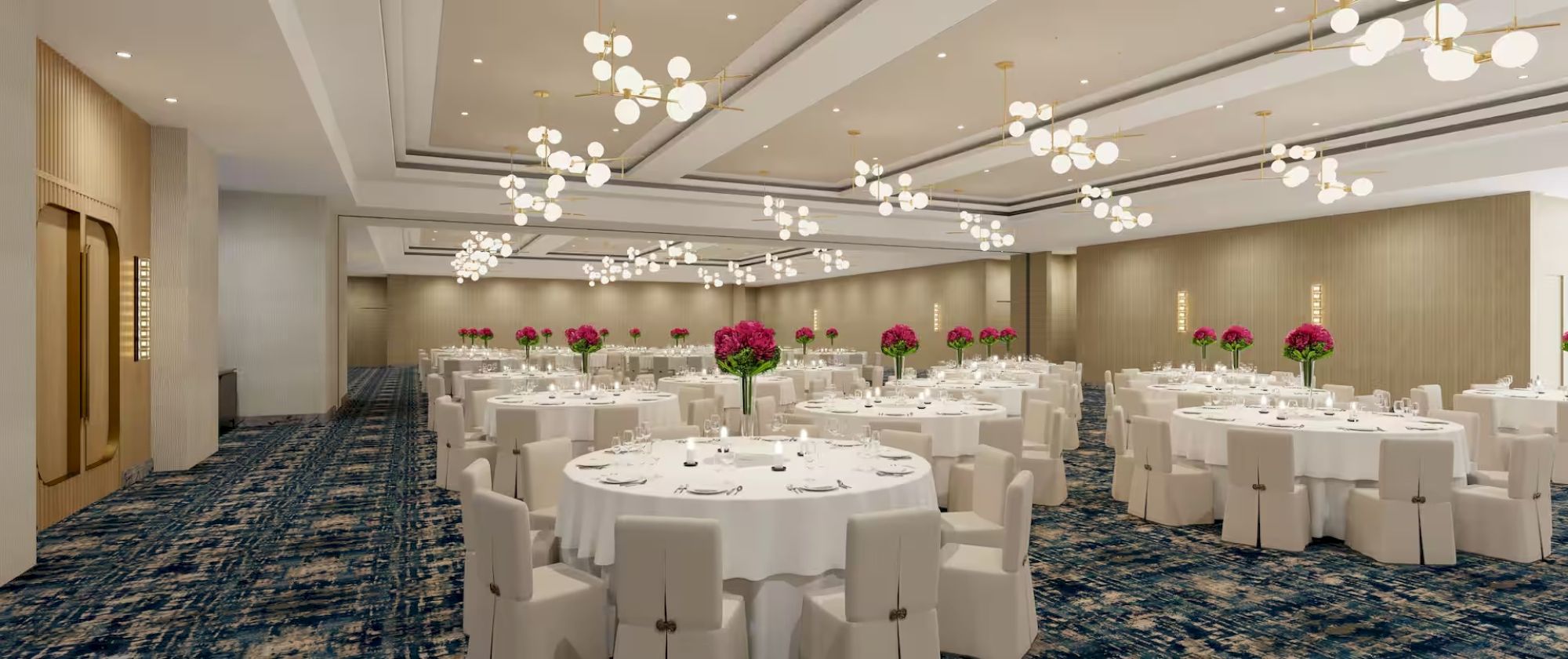 The image shows a spacious banquet hall with round tables set for an event, adorned with white tablecloths and floral centerpieces.