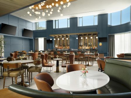 A stylish modern bar lounge with blue walls, hanging globe lights, tables, and a back counter stocked with spirits.