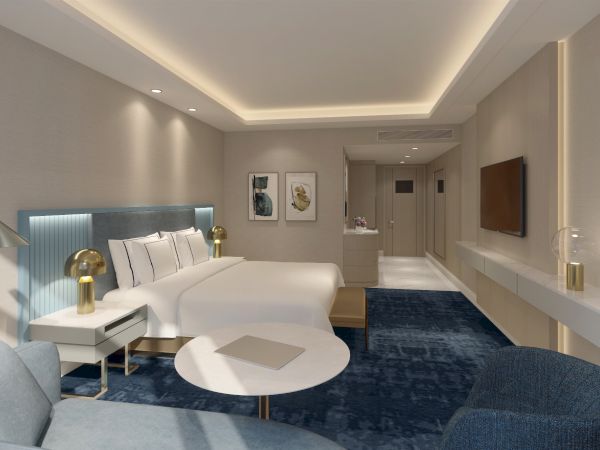 A modern hotel room with a large bed, blue carpet, sofa, coffee table, and wall-mounted TV under soft ambient lighting.