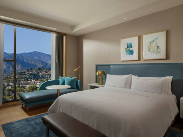 A stylish hotel room features a bed, seating area, and a window with a mountain view, decorated with art and accent lighting.