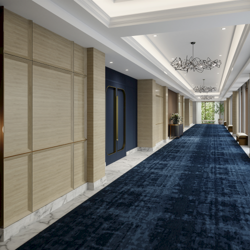 A modern corridor with a blue carpet, beige walls, chandeliers, and large windows at the end.