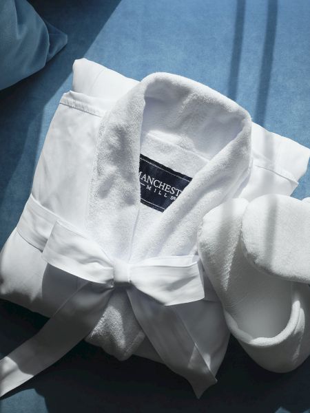 A white bathrobe with belt and sleeves on blue fabric, with a label reading Manchester Mills.
