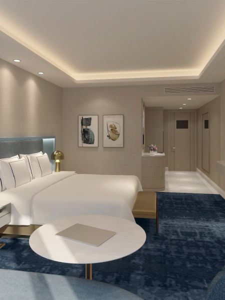 A spacious luxury hotel room with a king bed, blue carpet, modern seating, wall TV, and a bright, elegant desk area.