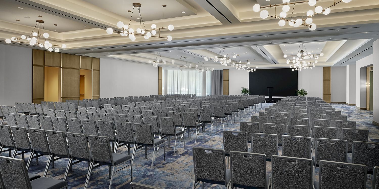 A modern conference room with rows of gray chairs, blue carpet, and hanging globe chandeliers over an empty auditorium.