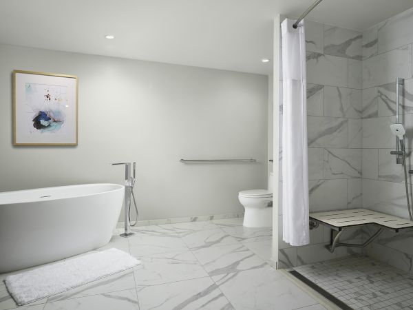 A modern bathroom with a white bathtub, marble tile walls, toilet, and a shower stall with a handheld showerhead.