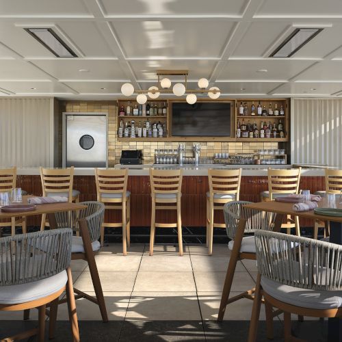 A modern outdoor patio bar with stacked bottles, a glassware display, and neatly set tables with chairs and lounge seating.